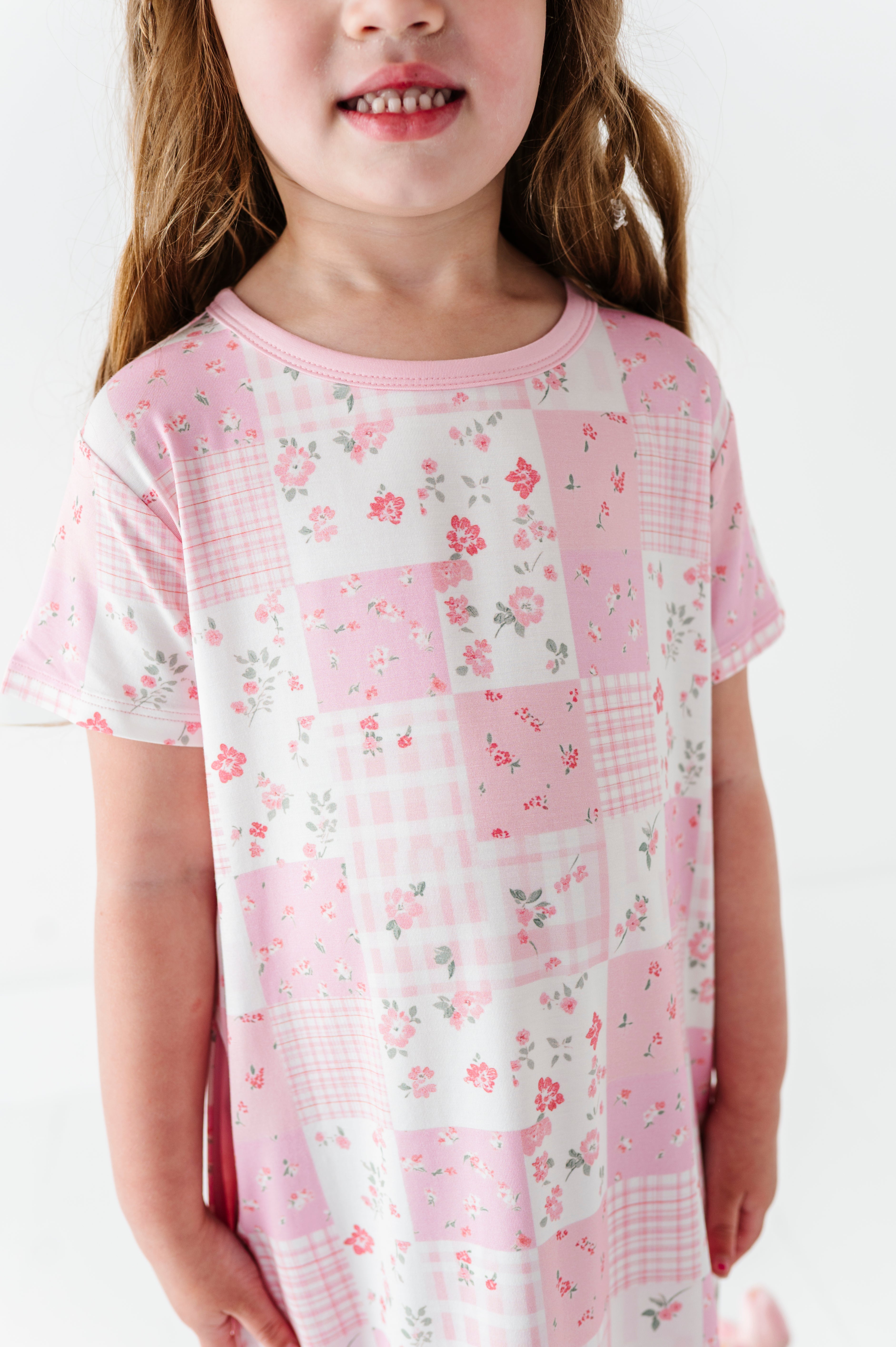 Young girl wearing a pink patchwork bamboo nightgown with floral patterns on a white background